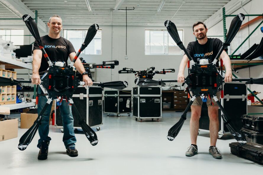 Two men holding drones that cover almost their entire height
