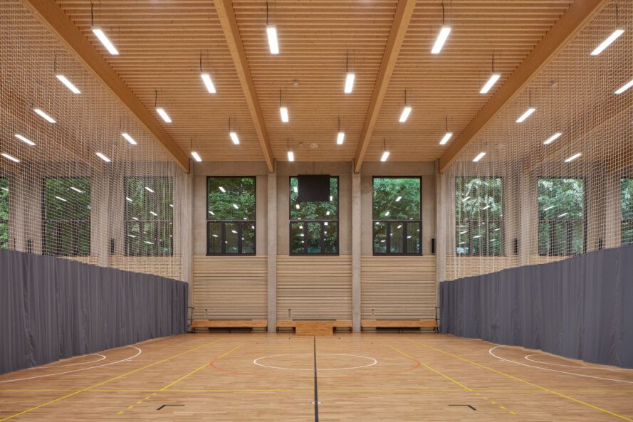 Court separated into three spaces with sports netting under a wood-clad ceiling with suspended lights