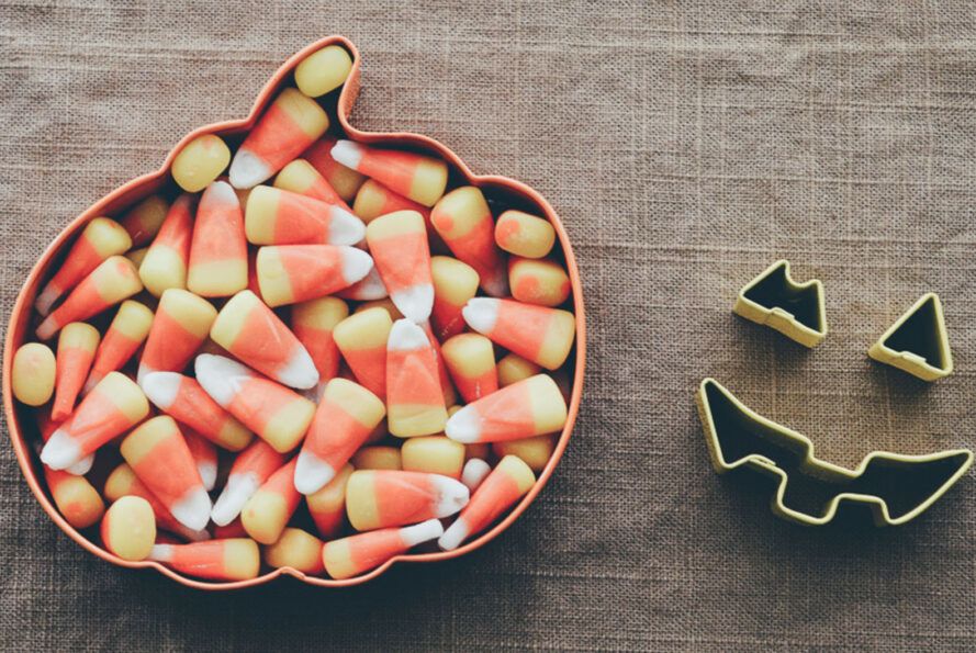 A pumpkin-shaped tray full of candy corn next to jack-o-lantern cookie cutters.