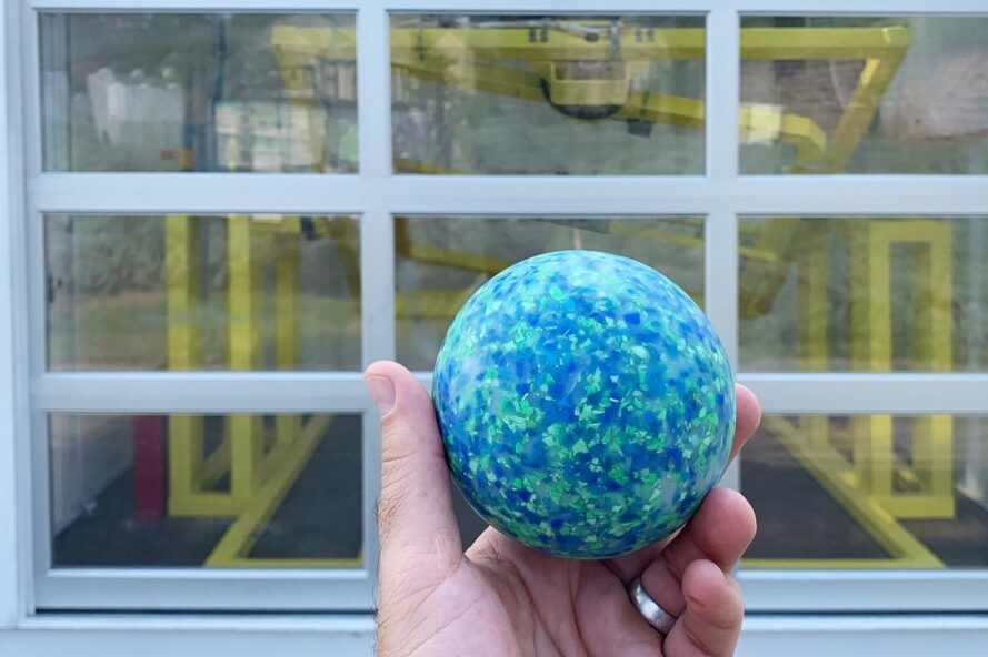 A hand holding a blue ball in front of a window